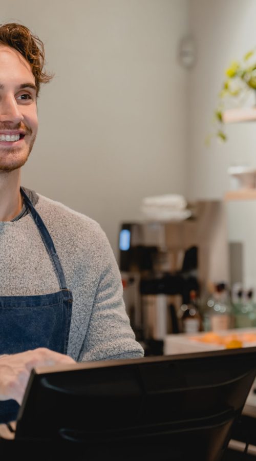 Smiling helpful young waiter servicing the customer at cash point in cafe
